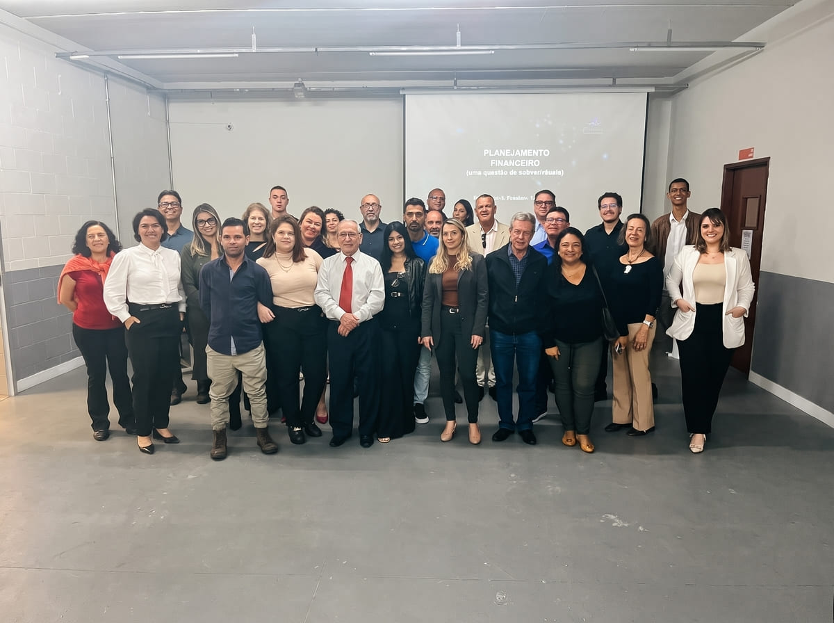 Foto em grupo de participantes de palestra sobre planejamento financeiro empresarial, reunidos em sala de treinamento com telão ao fundo, público diverso bem vestido, fotografia realista de evento corporativo